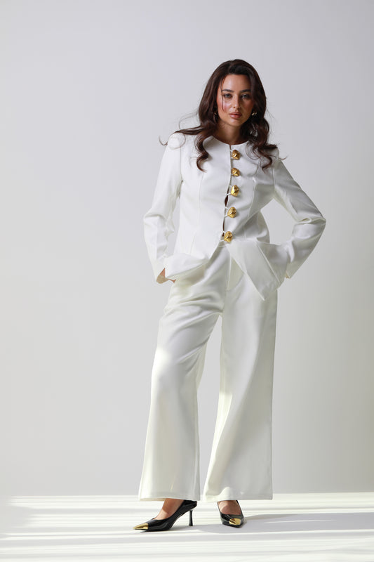 Woman wearing a white suit with gold buttons against a plain background